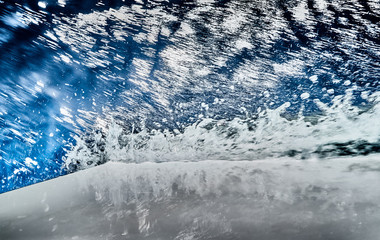 The nose of a sailing white boat cuts water, splashes spray, water glistens on the sunlight