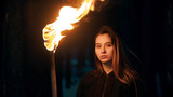 Fototapeta  - Young beautiful woman with torch in night forest looking in the camera