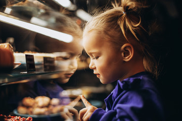 lovely girl admiringly examines a lighted showcase with various delicious cakes and desserts