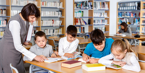 Wall Mural - Group of school kids studying in school library with friendly female teacher