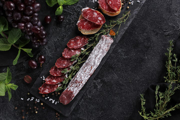 Wall Mural - The concept of Italian cuisine. Sausage with truffle on a black board with grape, mint, thyme and spices. Background image, copy space