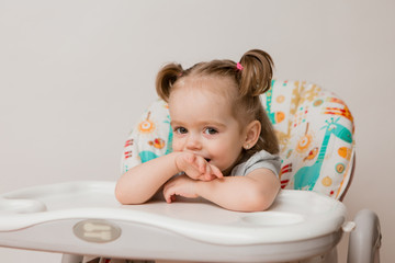 baby girl sitting in a child's chair eating fruit on a white background. baby food concept, space for text