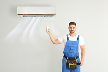 Male Technician Switching On Air Conditioner On Light Wall