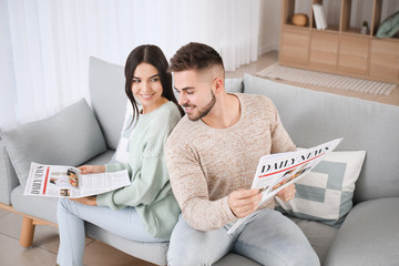 Sticker - Young couple reading newspapers while resting on sofa at home