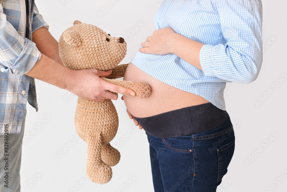 Beautiful pregnant couple with teddy bear on grey background, closeup