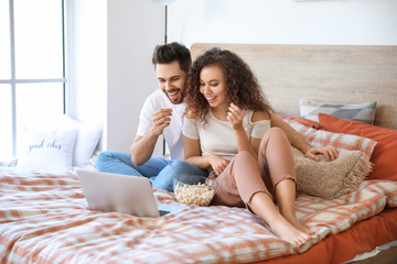 Wall Mural - Happy young couple watching movie in bedroom