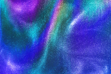 Abstract neon rainbow colored glitter particles flow with shallow depth of field underwater dust. Holiday disco magic shimmering under water festive party background. de-focused.