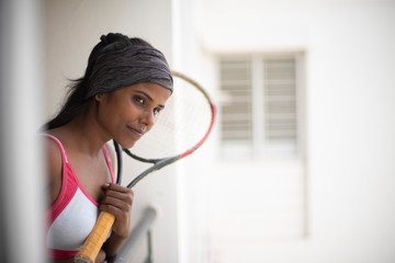 Wall Mural - Portrait of an attractive young brunette dark skinned Indian Bengali girl in western sportswear and a tennis bat in a balcony in white background. Indian lifestyle