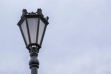 Vintage street lamp. Black paint with exfoliation. Background sky.