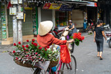 Fototapeta Kuchnia - The street vendor with bike loaded of flowers in old town street in Hanoi, old houses and street activites on background