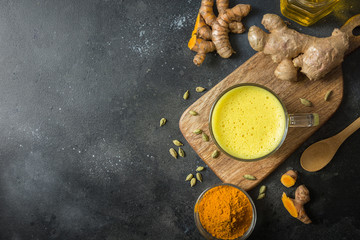 Wall Mural - Cup of Indian golden turmeric milk with curcuma powder and ingredients on black. View from above.