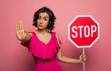 Beautiful stylish serious young woman in a pink dress shows a big red sign of 