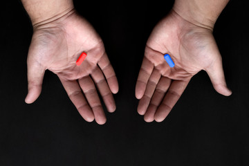 Red and blue pills on hand on black background. Red pill blue pill concept.