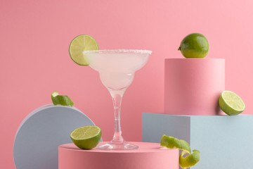 Glass of Margarita cocktail and fresh limes on pink background