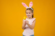 © producer - happy cute little child girl with pink bunny ears holding painted Easter eggs on studio yellow background. Easter day