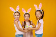 © producer - happy little child girls with pink bunny ears holding basket with painted Easter eggs on studio background. Easter day