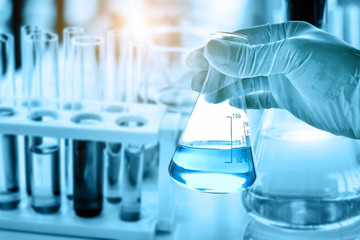 Wall Mural - hand of scientist holding flask with lab glassware in chemical laboratory background, science labora
