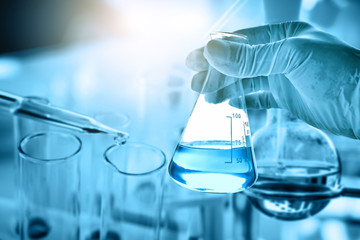 Wall Mural - hand of scientist holding flask with lab glassware in chemical laboratory background, science labora