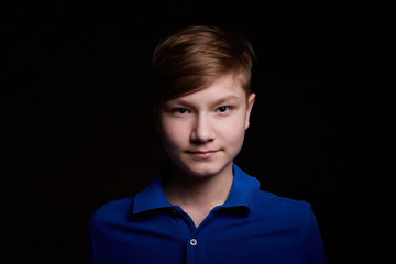 Low key portrait of a handsome brunette young male teenager in blue t-shirt. Interesting boy and dark background with blue light