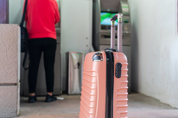 Travel luggage with a woman drawing money from ATM on background. Vacation financing, travel money concept