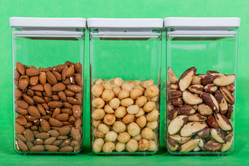 Three plastic containers with nuts, one with nuts, one with macadamias and the third with brazil nut raw on a green background