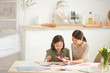 © AnnaStills - Horizontal shot of happy young woman and teen girl sitting together at table in spacious room working on holiday cards together, copy space