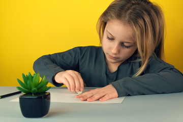 Selective focus.Adorable captured little girl with focused face erases the drawn at table decorative flower in black pot on yellow background.Concept of paint children, development of artistic taste