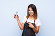 © luismolinero - Young woman over isolated blue background with hairdresser or barber dress and pointing it