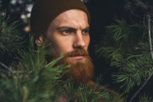 Portrait Brutal Bearded Hipster Man In The Forest. Brutal Brunette Bearded Man In Warm Hat In The Woods On A Background Of Trees Bearded Young Man Confident