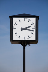 white-black old antique railway station clock with hour and minute hands in front of a blue sky, vertical format, by day