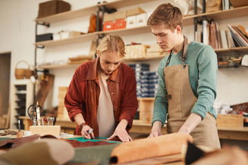 Wall Mural - Horizontal medium shot of young Caucasian man and woman working together in modern leather craft workshop