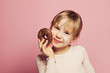 © millaf - Smiling little girl holding chocolate donut. Pretty Child girl on pink background