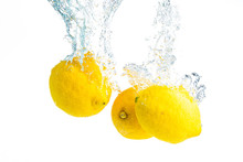 Lemons Splash Into Water And Sinking On White Background.