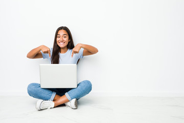 Young mixed race indian woman sitting working on laptop points down with fingers, positive feeling.