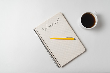 Notepad with the words Wake up on white background. Copybook with pen and morning coffee