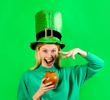 Smiling Blonde Girl In Leprechaun Costume Holds Pot With Gold. Green Hat. Leprechaun. Pot With Gold. Green Leprechaun. Hat With Clover. Saint Patrick's Day. Irish Traditions. Saint Patrick.