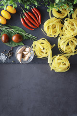 Wall Mural - Pasta on the table with spices and vegetables. Noodles with vegetables for cooking on a black stone background.