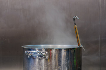 Steam over stainless cooking pot with metallic background over cooking station in kitchen of restaurant.