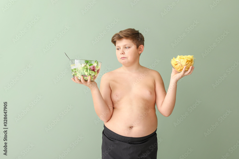 Overweight boy choosing between salad and chips on color background