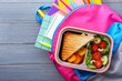 Lunch box and schoolbag on wooden background