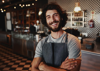 Portrait of smiling handsome young waiter standing at coffee shop