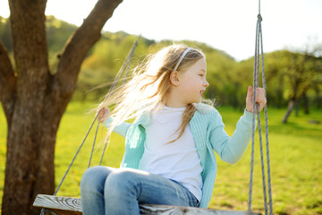 Wall Mural - Cute little girl having fun on a swing outdoors in summer garden. Summer leisure for kids.