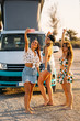 © ManuPadilla - Group of three surfer women friends making a selfie with a camper van in the beach during a summer day.