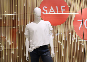 Mannequin in a shop window. Mannequin in a white T-shirt and jeans behind a glass store.