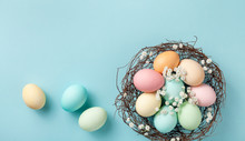 Pastel Easter Eggs In Nest On Blue Background Top View. Flat Lay Style.