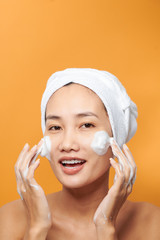 Wall Mural - Laughing girl applying moisturizing cream on her face. Photo of young girl with flawless skin on orange background. Skin care and beauty concept