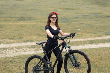 Girl on a mountain bike on offroad, beautiful portrait of a cyclist at sunset, Fitness girl rides a modern carbon fiber mountain bike in sportswear. Close-up portrait of a girl in a helmet and glasses