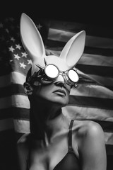 woman in white rabbit mask and biker glasses on american flag background black and white