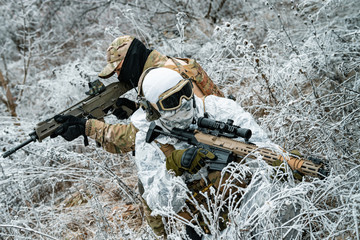 Wall Mural - Two men in camouflage white, green uniform with machineguns back to back. Soldiers with muchinegun stood on knelt in the winter grass.