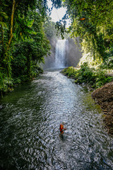 A woman catching freshwater fish in a river. In the background is the majestic Hikong Alu waterfalls of Lake Sebu, South Cotabato, Philippines.